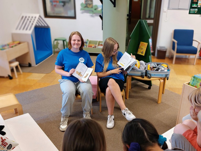 två ungdomar i blå tröjor läser för barn